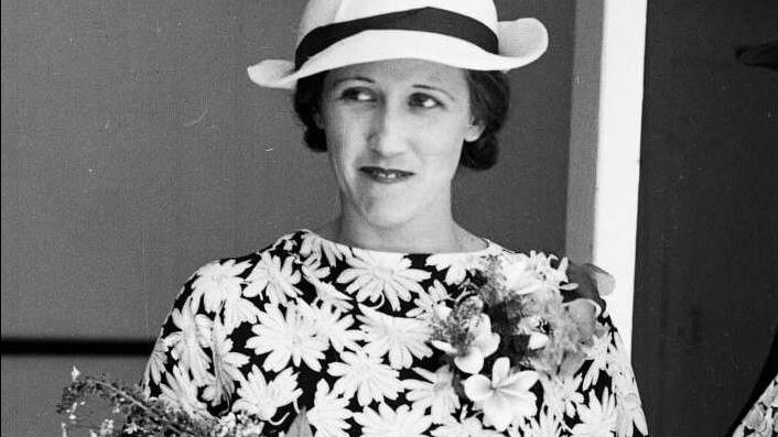 An old black and white photo of a woman in a floral dress and white hat 