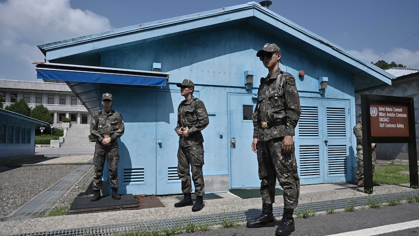 South Korean soldiers stand guard in front of a blue building in the DMZ.