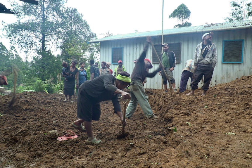 Local people dig at the site where a house was buried by mud and dirt