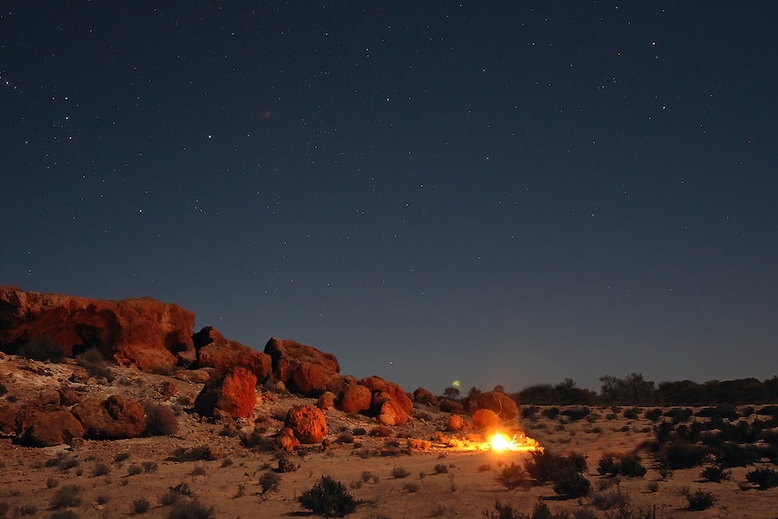 A small camp fire against some granite rocks and the night sky