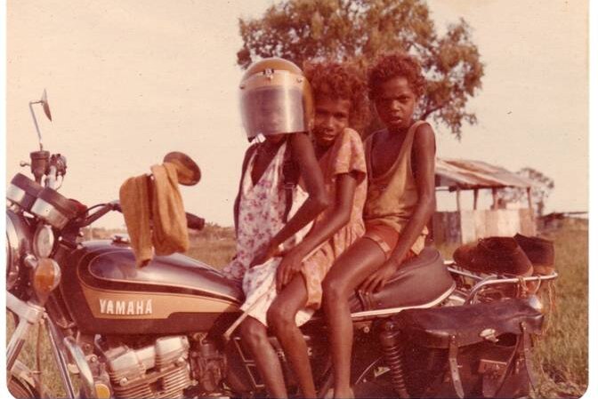 Three Gurindji kids sitting on Rob Wesley-Smith's motorbike.