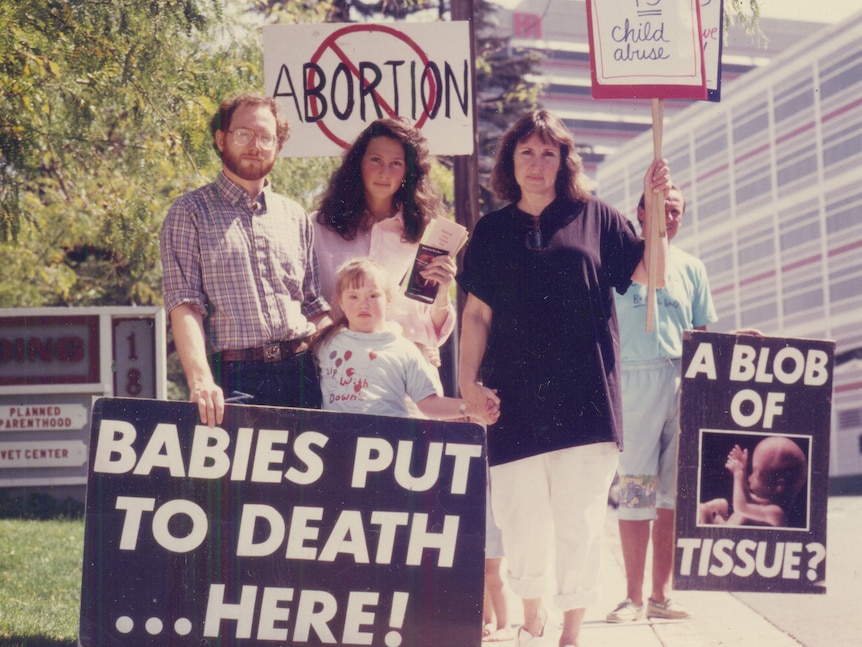 A retro image shows a mother, father and two children holding signs. 