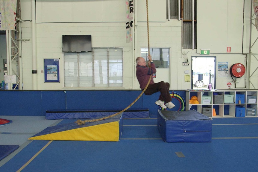 Ken Orford swings from a rope in a gym.