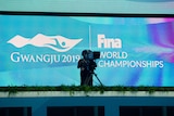 A TV cameraman stands in front of a big screen with a sign for FINA's world swimming championships.