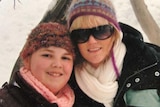 young girl with beanie and scarf smiling next to blonde woman with glasses and snow jacket