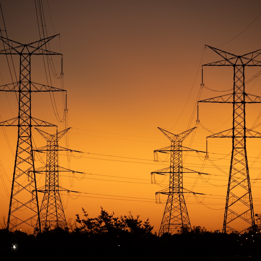 Powerlines suspended between towers against orange dusk  sky.