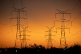 Powerlines suspended between towers against orange dusk sky.