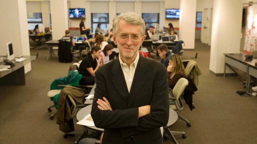 Man standing with his arms folded as a table of young adults sits behind him.