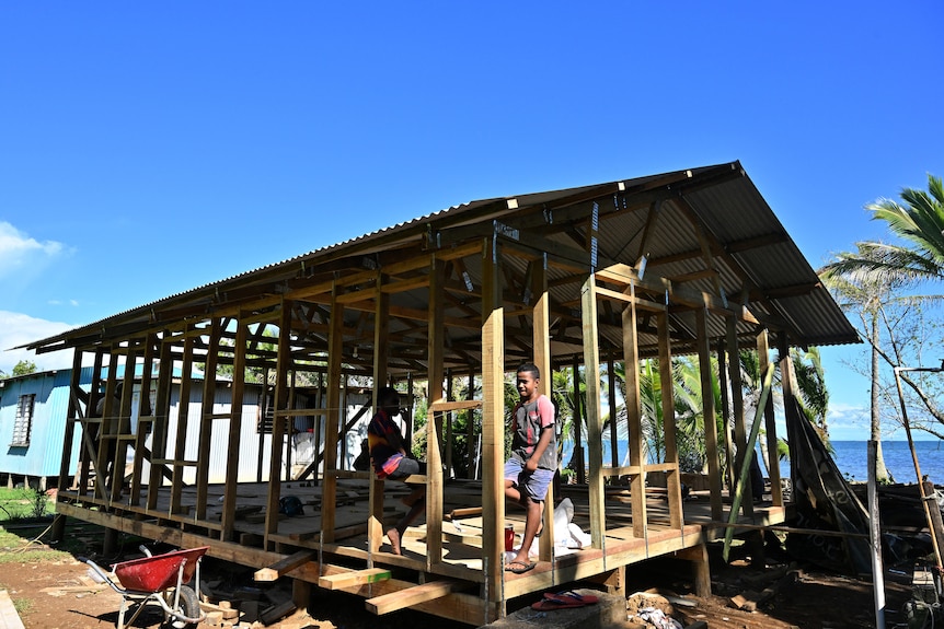 a child leans against the posts of a house being built high up from the water in Fiji