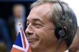 Nigel Farage looks smug while wearing headphones