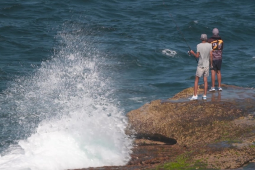 two people fishing in the sea while standing on rocks