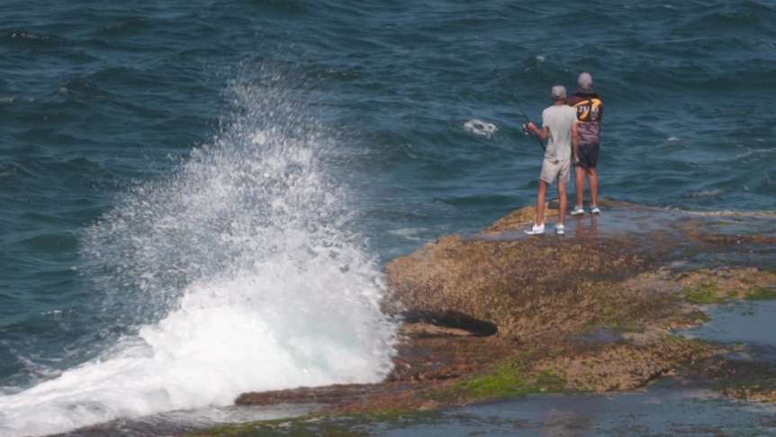 two people fishing in the sea while standing on rocks