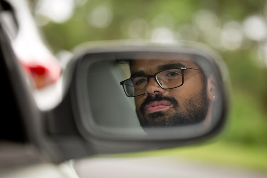 Arpit Charwal looks in the side mirror of his car while driving.