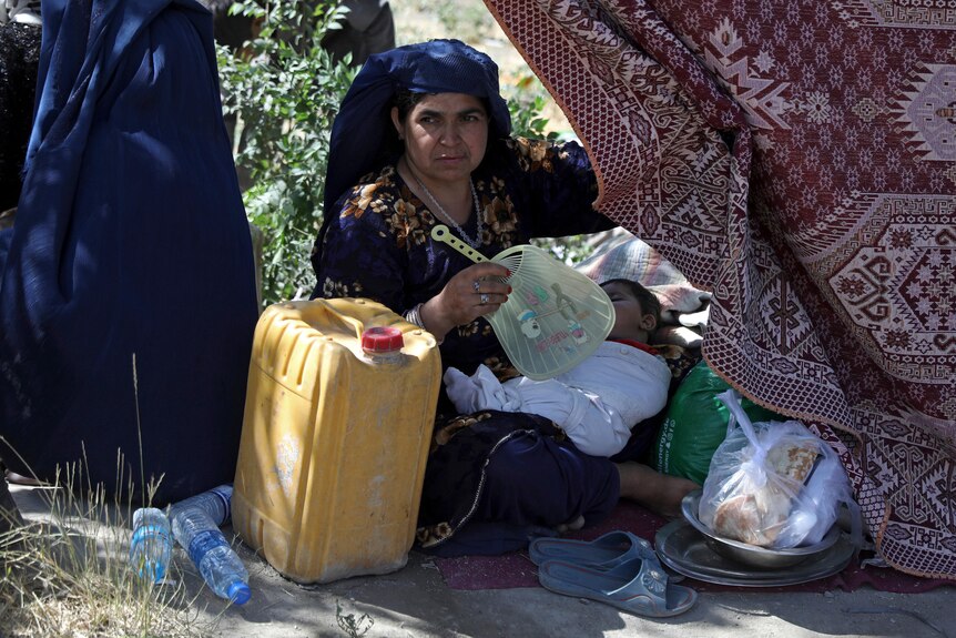 An Afghan woman sits on the ground with a sleeping child in her lap. 