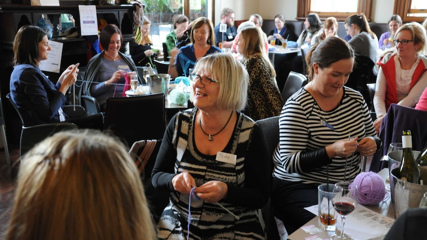 Large group of women sitting around tables in a pub knitting.