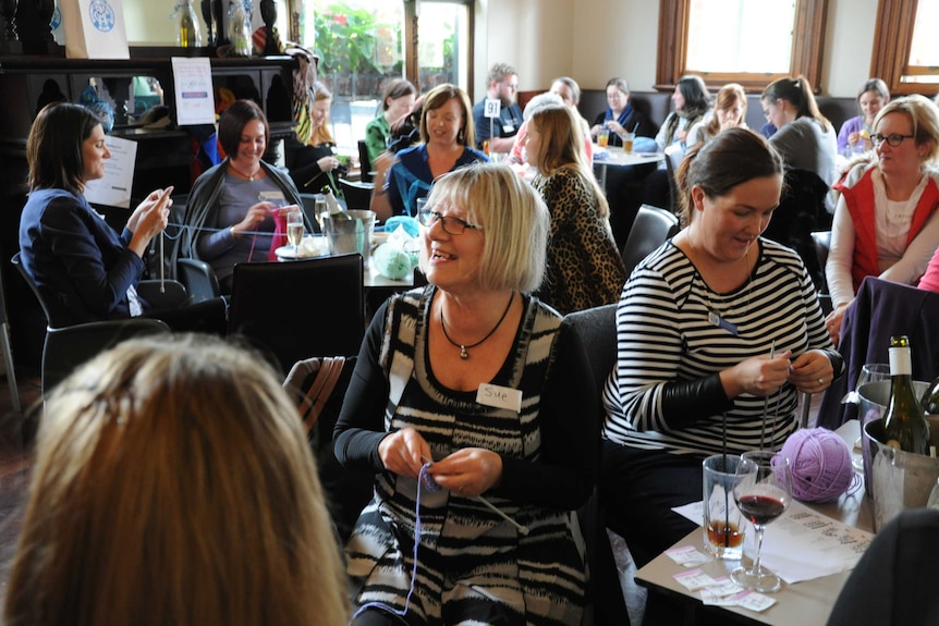 Large group of women sitting around tables in a pub knitting.