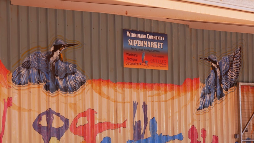 A brightly-painted building wall with a sign hanging that reads 'Wirrimanu community supermarket'.