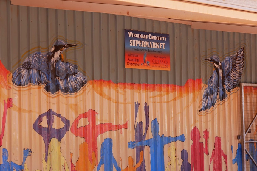 A brightly-painted building wall with a sign hanging that reads 'Wirrimanu community supermarket'.