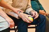 A young carer places her hand on the arm of a older man, holding a stress ball.