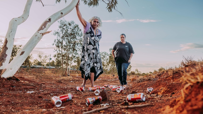 Two Aboriginal women in a dry creek bed looking at empty beer cans.