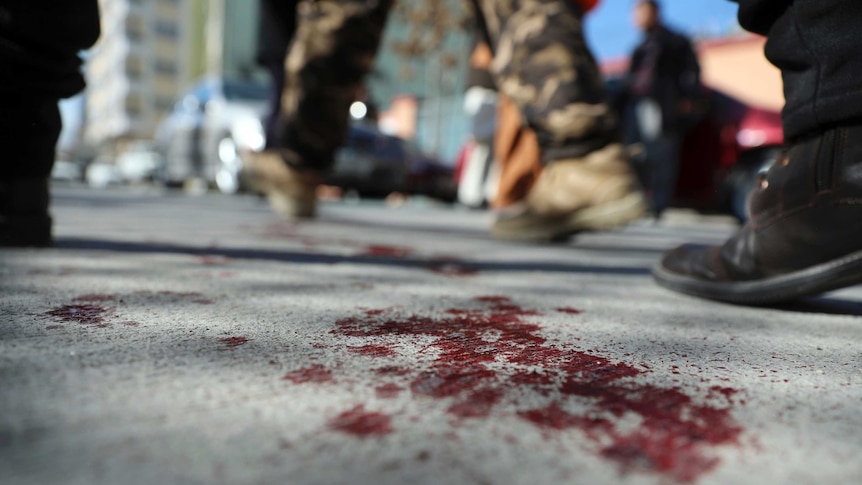 Afghan security personnel walk on a bloodstained road