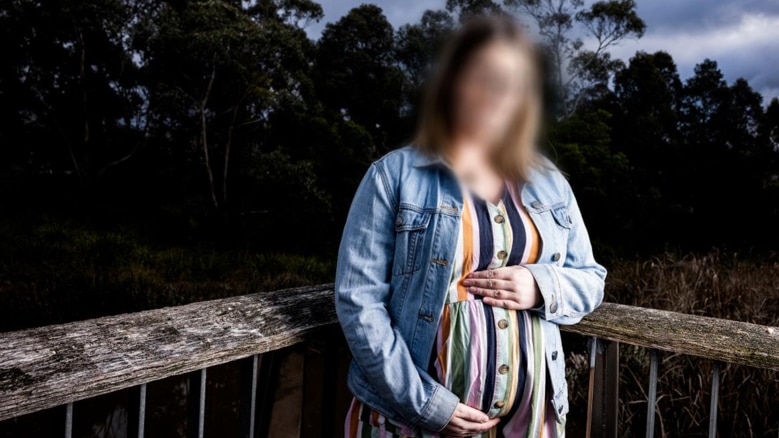 Pregnant woman with face blurred, holding her baby bump.