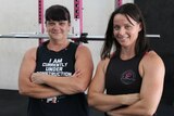 Two dark-haired women standing in a gym.