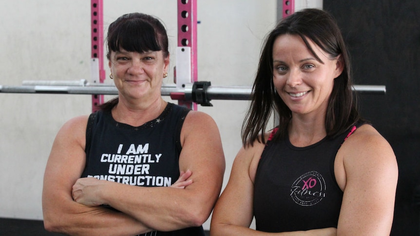 Two dark-haired women standing in a gym.