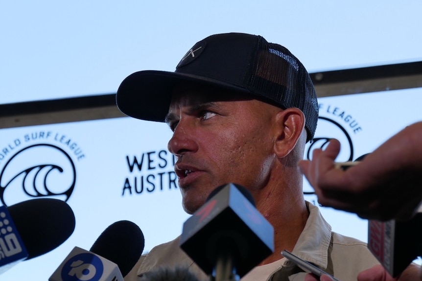 A low angle shot of a man with a hat on who is being questioned by the media.