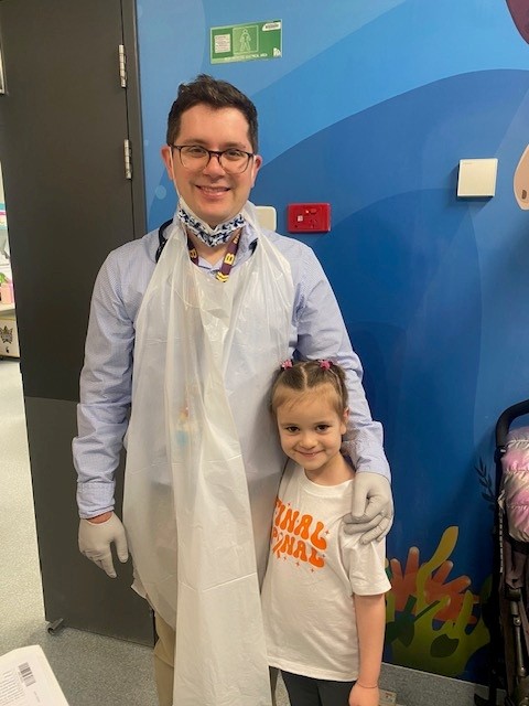 Un médico de mediana edad con una bata de hospital rodea con el brazo a una niña en un centro médico