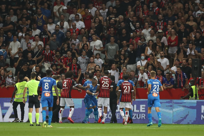 Un joueur en chemise bleue jette une bouteille vers un groupe de supporters dans un stand