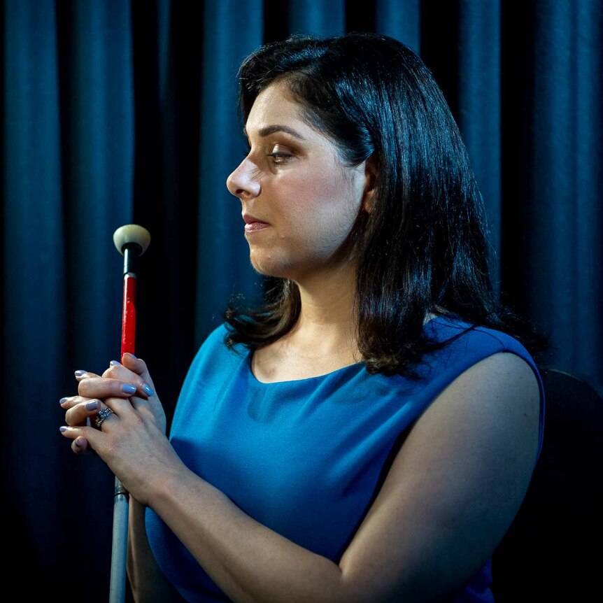 A photo of Nas Campanella against a blue curtain holding her cane.