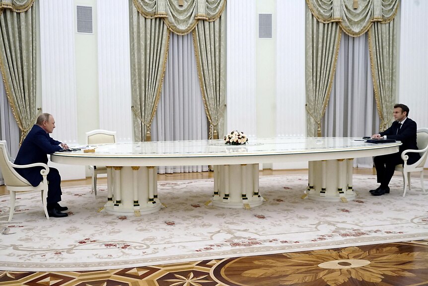 Vladimir Poutine et Emmanuel Macron sont assis aux extrémités opposées d'une longue table au Kremlin.