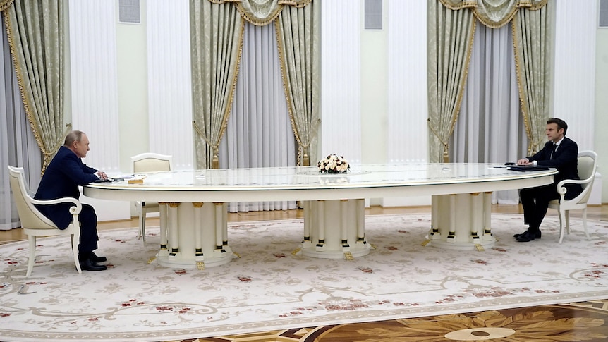 Vladimir Putin and Emmanuel Macron sit at opposite ends of a long table at the Kremlin.