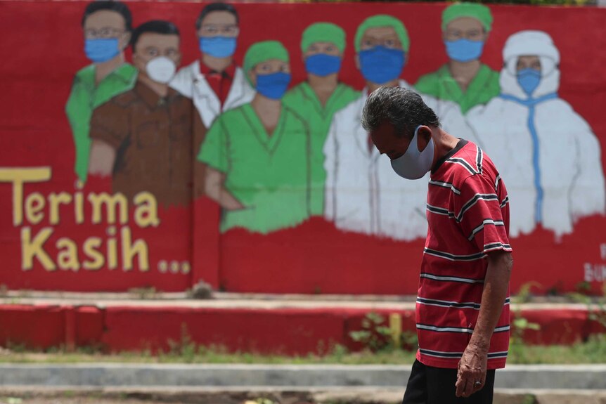 A man wearing a face mask walks past a coronavirus-themed mural in Jakarta.