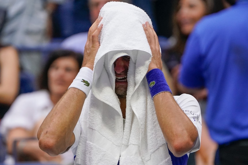 Novak Djokovic cries with a white towel over his head