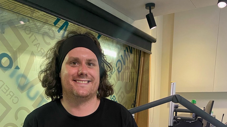 A portrait photograph of Dr Aaron Raynor in a radio studio
