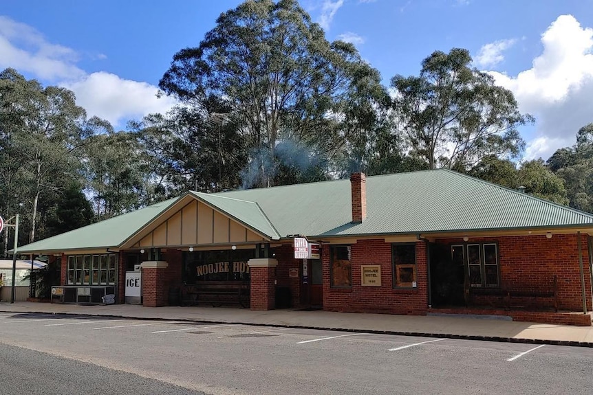 Red Brick building with green roof with a noojee hotel sign on the front window, behind are large trees and a blue sky