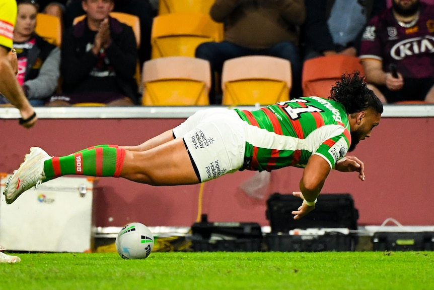 A South Sydney NRL player goes parallel to the ground after planting the ball for a try.