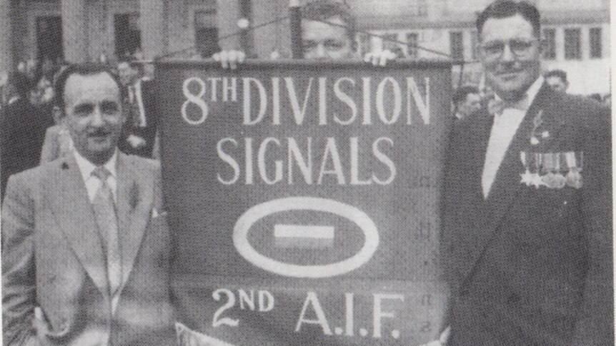 Three men holding a unit banner for the 8th division signals in an ANZAC day parade