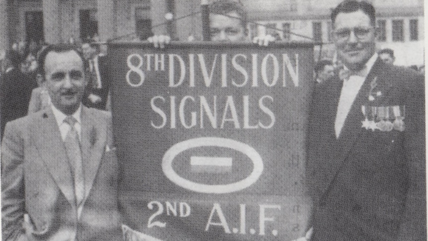 Three men holding a unit banner for the 8th division signals in an ANZAC day parade