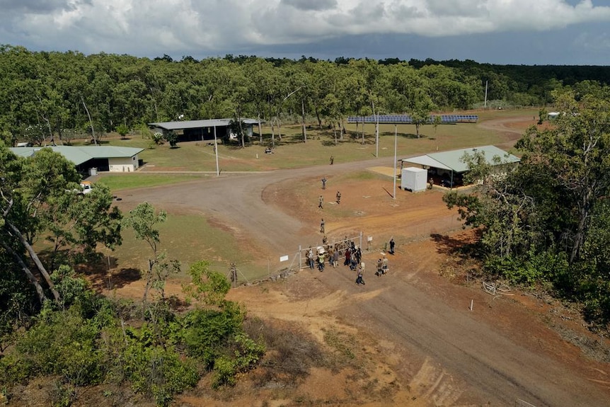 An aerial image of two groups gathered on opposing sides of a cyclone fence, in a compound in the bush