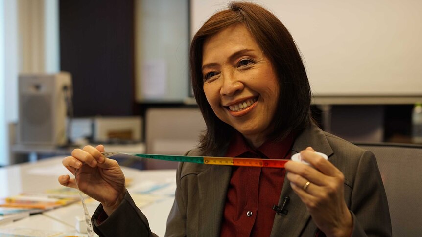 A woman wearing a smart jacket smiles as she holds up a tape measure.