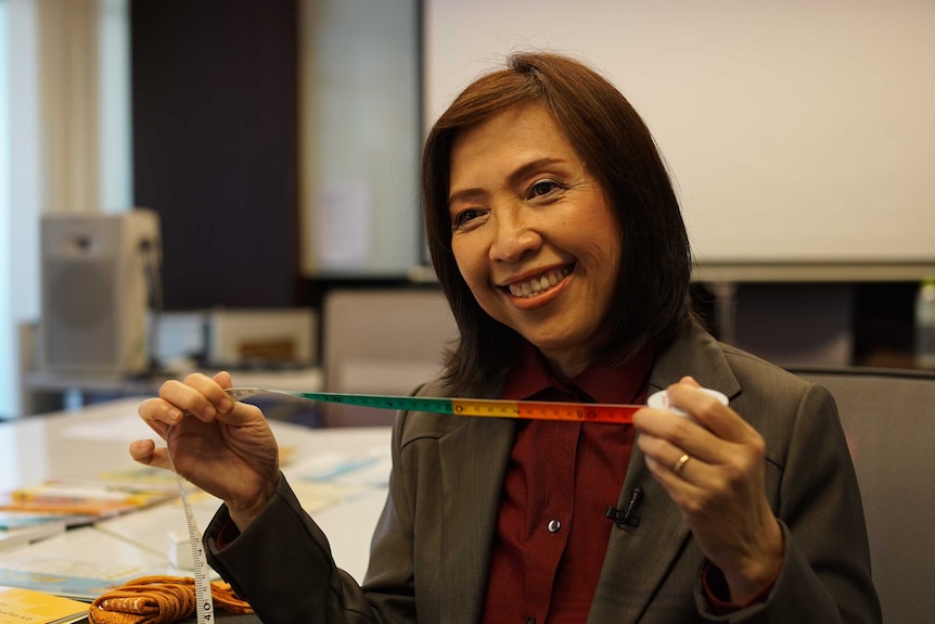 A woman wearing a smart jacket smiles as she holds up a tape measure.