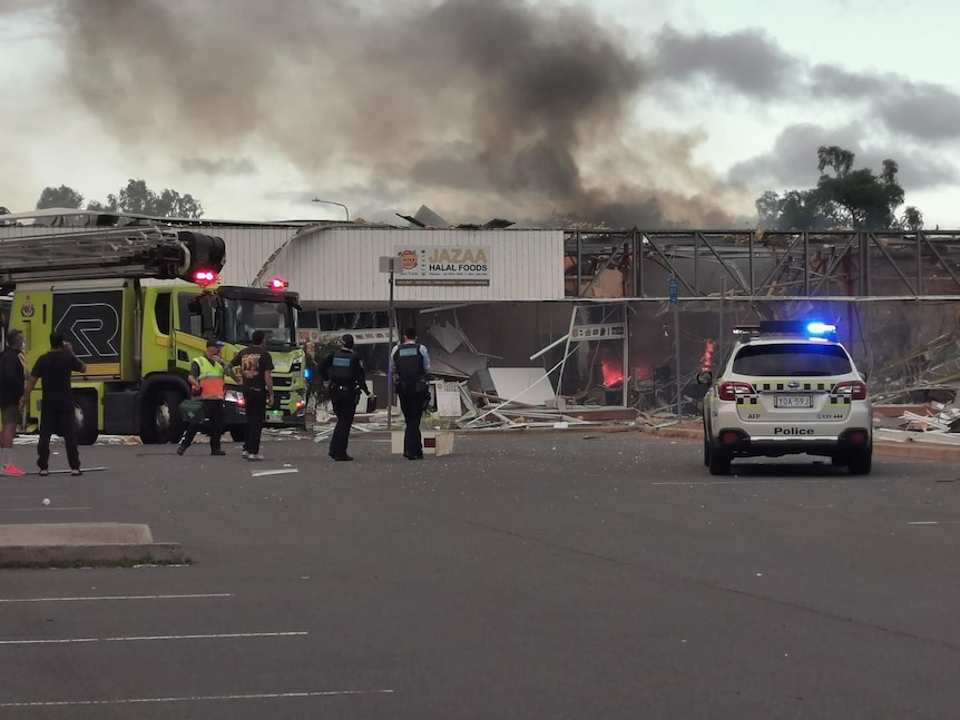 A gutted store on fire with police and a fire truck outside.