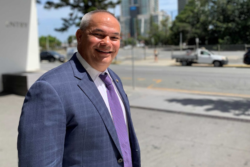 Man smiling at camera with highrise tower behind him