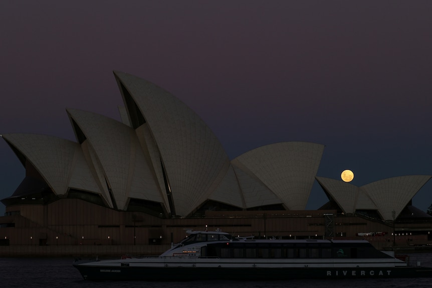 A bright red full moon is visible behind the Sydney Opera House