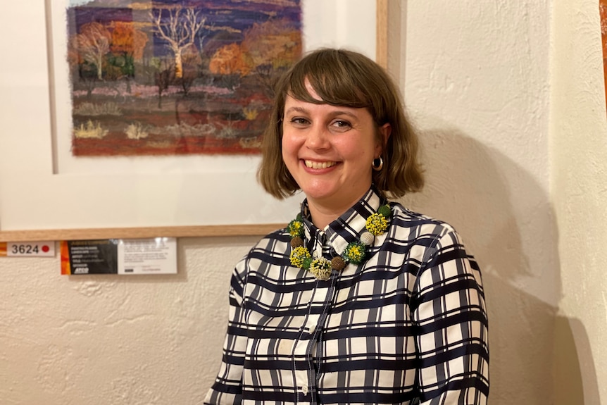 A woman smiling, standing in front of a winning artwork.