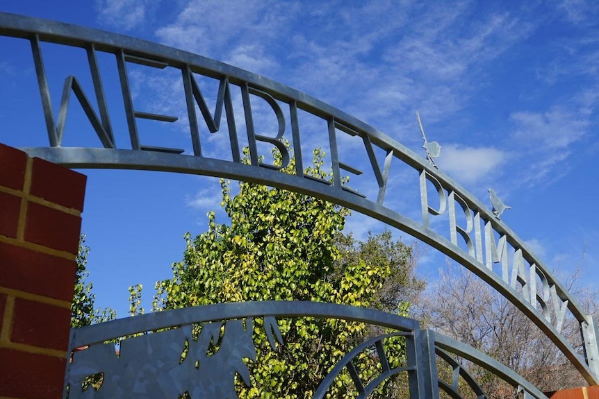 A wrought iron sign reading Wembley Primary School atop gates with blue sky in the background.