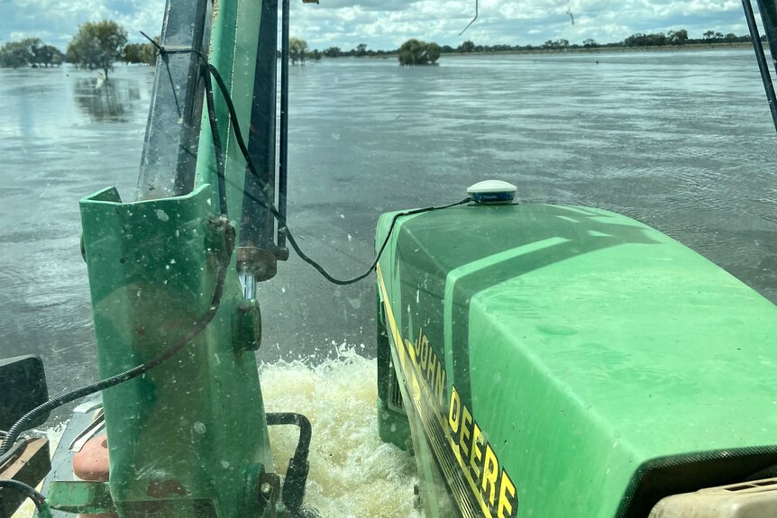 A John Deere tractor drives through floodwater.